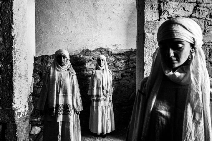 Three women wearing the local costumes of Kallimasia in Chios, inside an old abandoned local house.