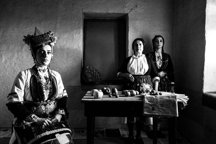 Three women wearing the local dresses of the villages of the valley of Naoussa, inside a local house by the window
