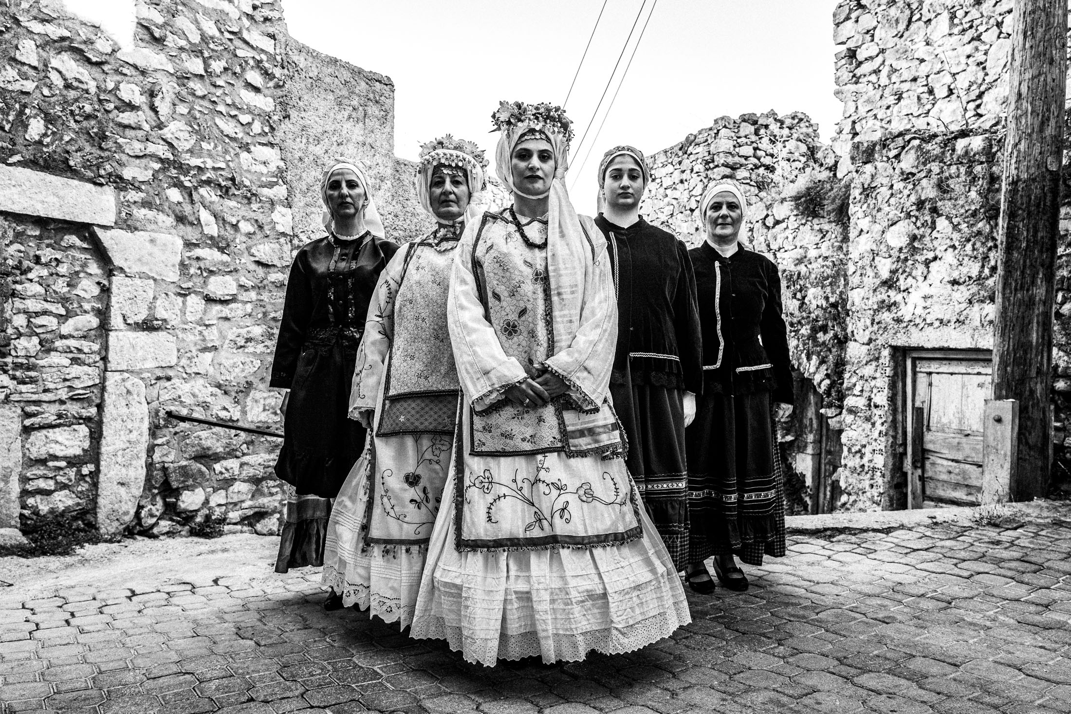 Five women wearing the local costumes of Agios Georgios Sykoussis, standing in formation inside the village
