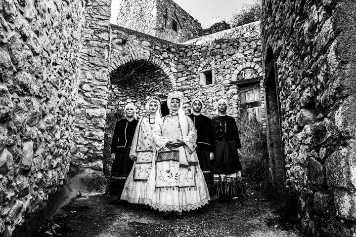 Five women standing in formation around the village of Agios Georgios Sykoussis, wearing the local costumes