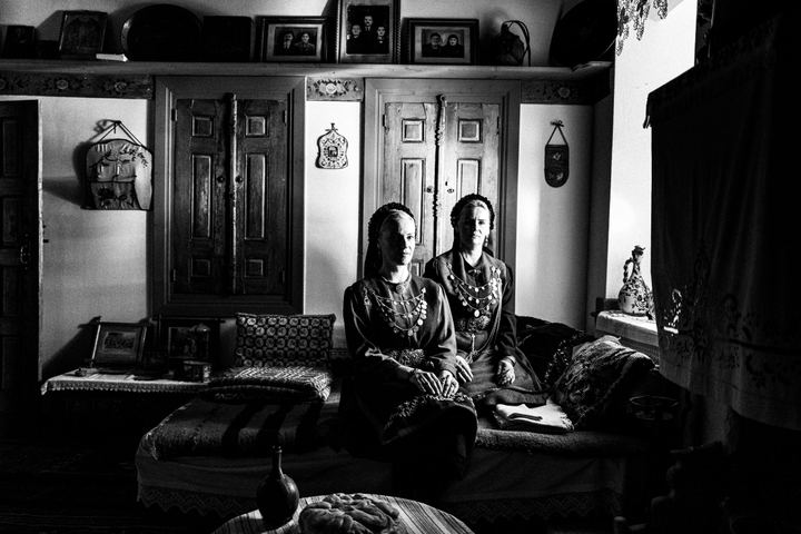Two women wearing the kamvounia costumes, sitting inside a traditional mansion in Siatista, by the window