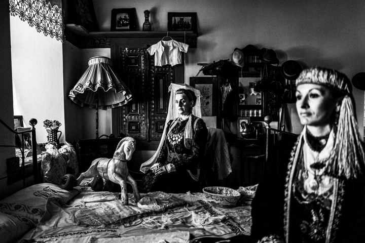 Two women wearing the urban attire of Kozani, sitting inside a traditional mansion in Siatista, among numerous props