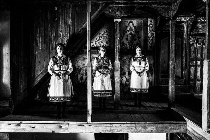 Thee women standing in line facing the camera, wearing the costumes of Tsartsampas, inside a traditional mansion in Siatista.