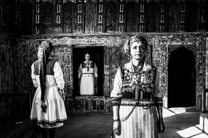 Three women in a peculiar formation, wearing the traditional costumes of Tsartsampas, stand inside a traditional mansion in Siatista
