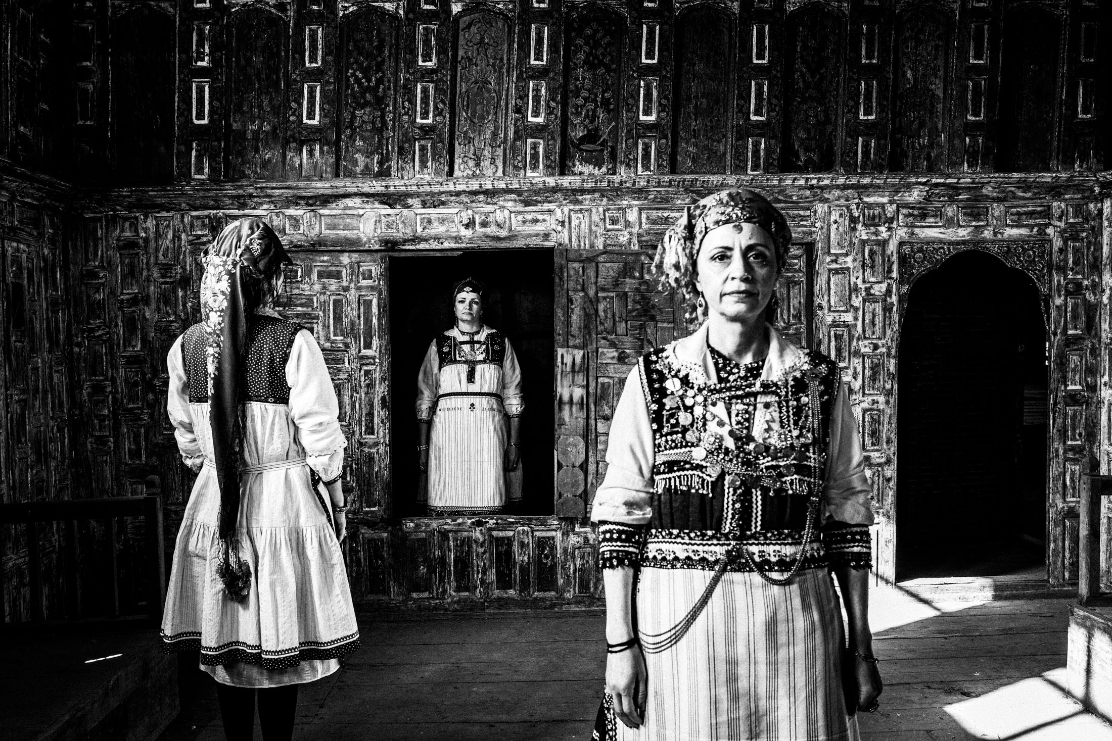 Three women in a peculiar formation, wearing the traditional costumes of Tsartsampas, stand inside a traditional mansion in Siatista