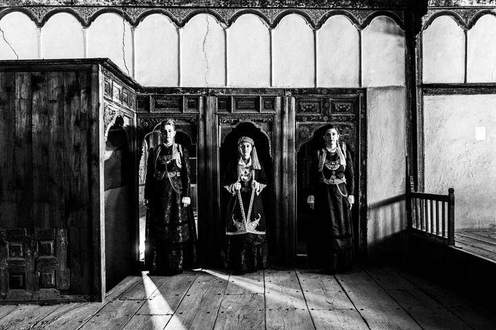 Thee women standing in line facing the camera, wearing the urban costumes of Kozani, inside a traditional mansion in Siatista.