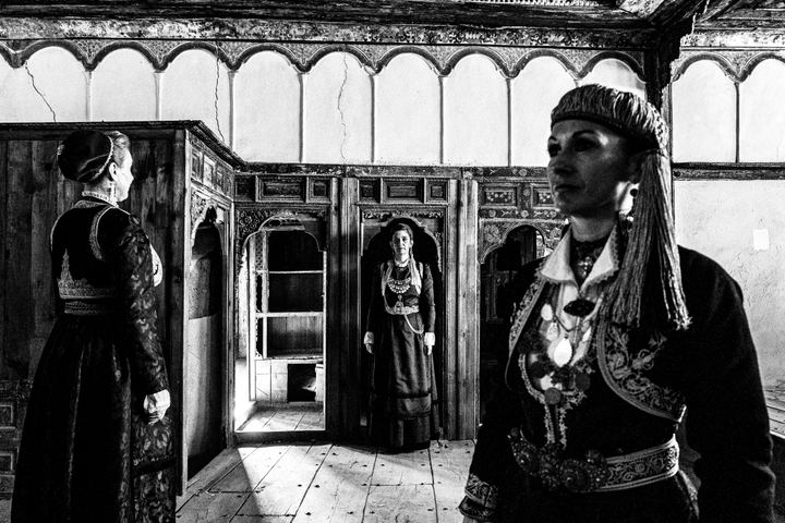 Three women wearing the urban dresses of Kozani, standing inside a traditional mansion in Siatista