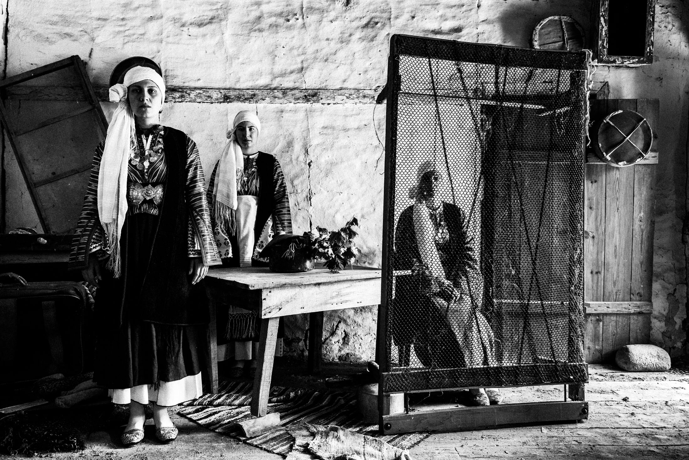 Three women wearing the local costumes of Vamvakou, inside a local warehouse.