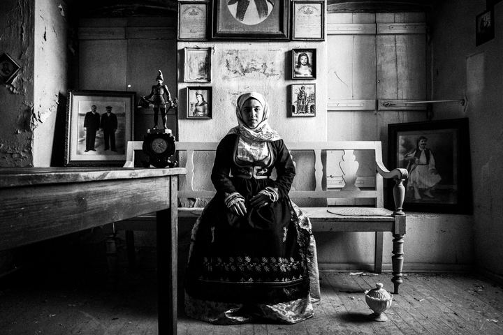 A woman wearing the traditional costume of Geraki, Laconia, sitting inside an old abandoned local house