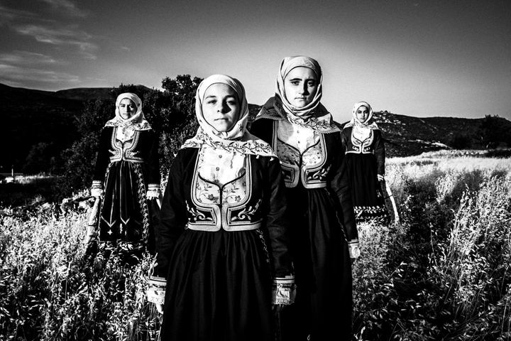 Women wearing the local costumes of Geraki in the Peloponnese, standing inside a local wheat field