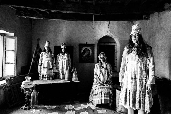 Four women wearing the local dresses of Thymiana standing inside an old local house by a window and religious icons