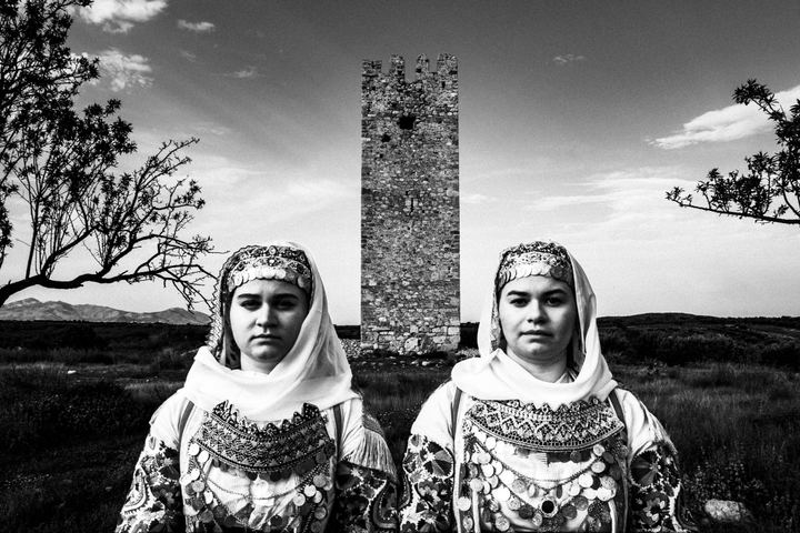 Women wearing the costumes of Markopoulo, Attica standing outside a local tower