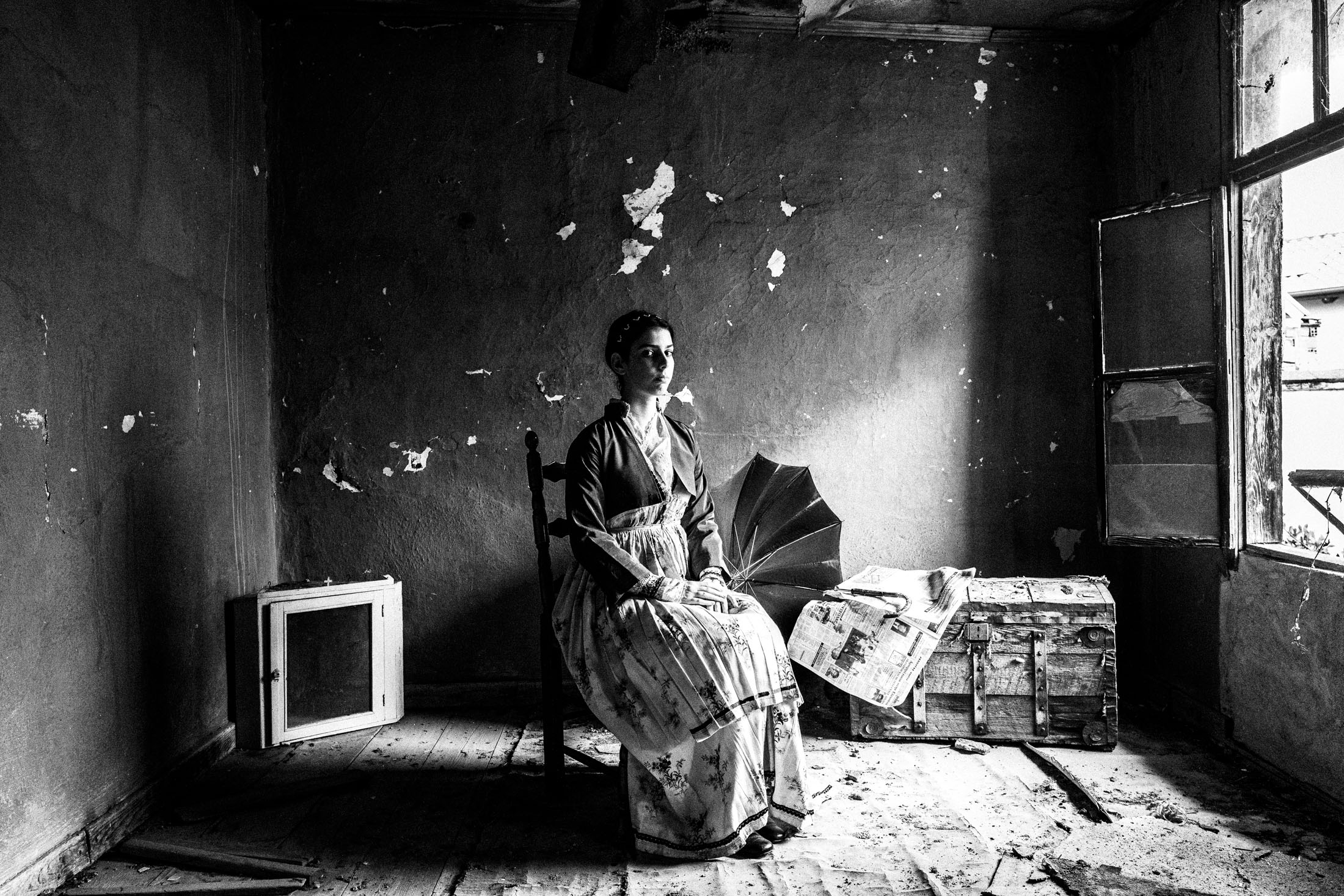 A woman wearing the urban dress of Veria, Imathia, Macedonia, sittign on a chair, in a local abandoned house