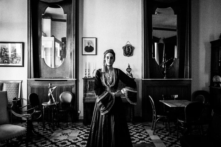 A woman wearing the urban Amalia costume, standing inside a traditional cafe in Tripolis, Peloponnese