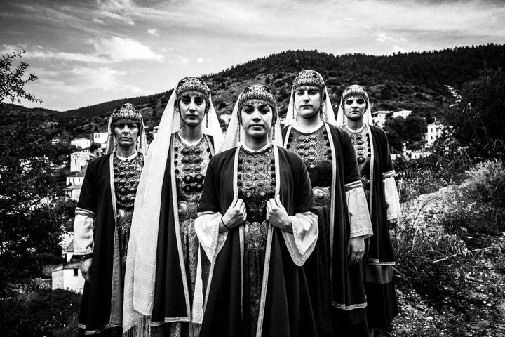 Five women wearing the local costumes of Prastos, Arcadia, standing in formation overlooking the village.