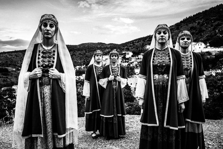 Women wearing the local costumes of Prastos in the Peloponnese, standing atop a local rooftop