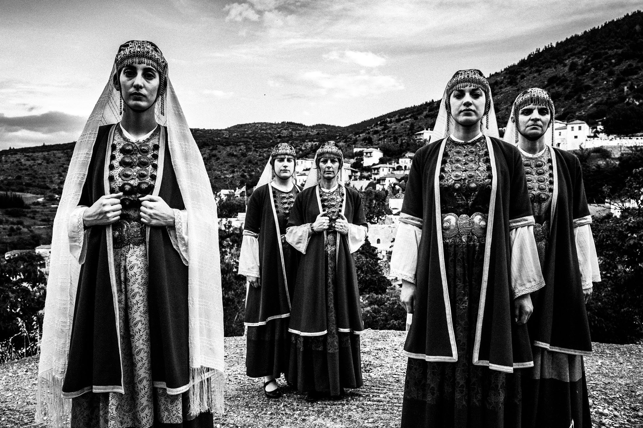 Women wearing the local costumes of Prastos in the Peloponnese, standing atop a local rooftop