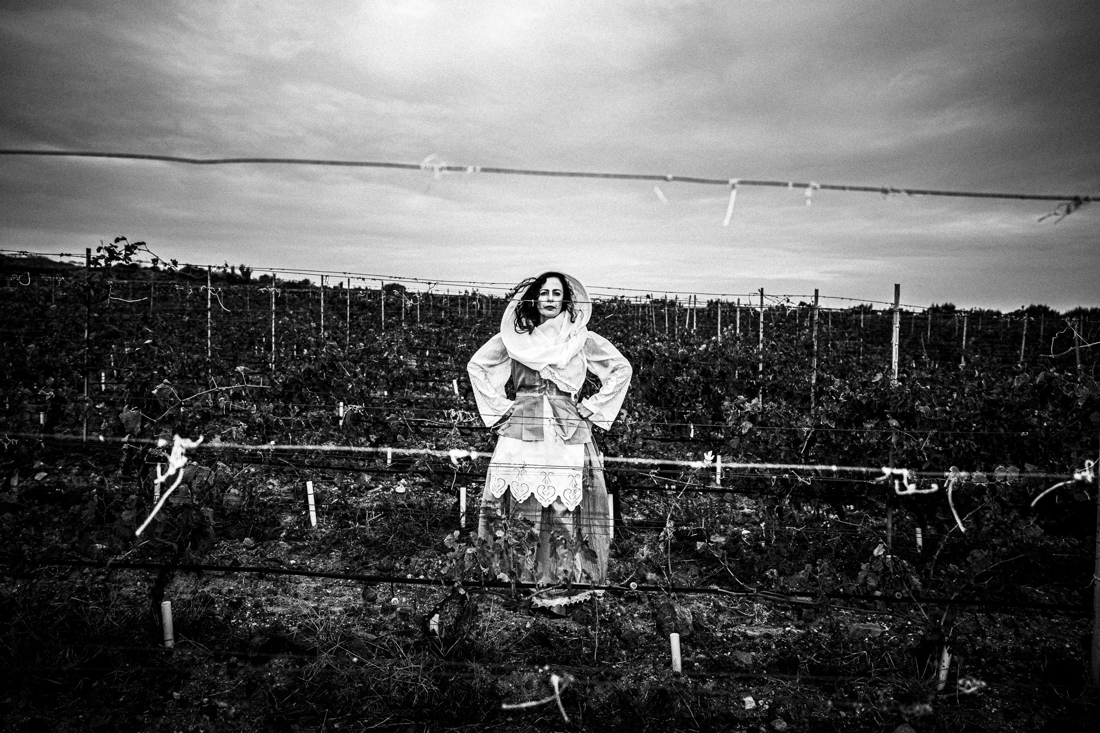 A woman wearing the local dress of Santorini, standing in a vineyard in Oia