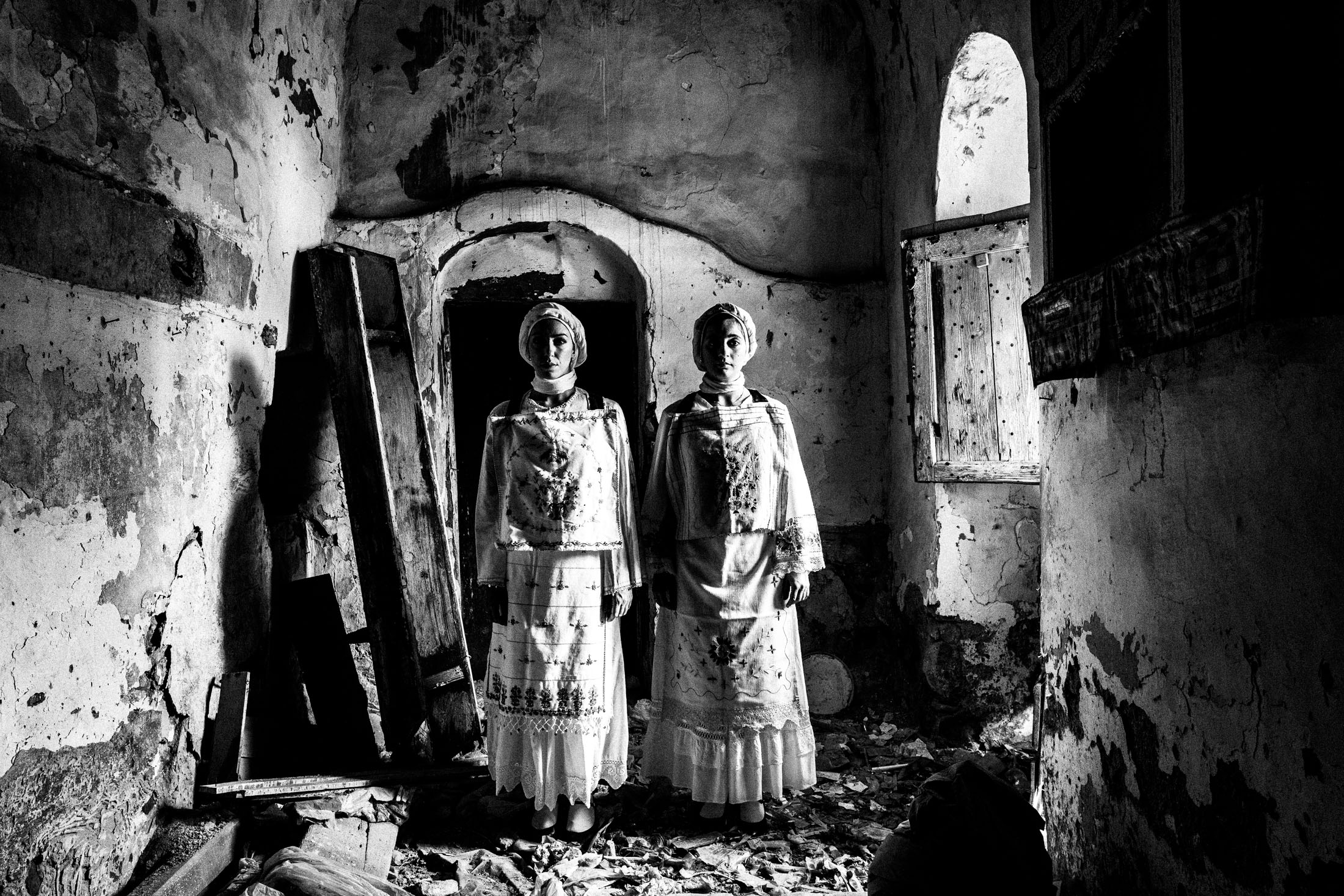 Two women wearing the local costumes of Lithi, standing side by side inside a local house