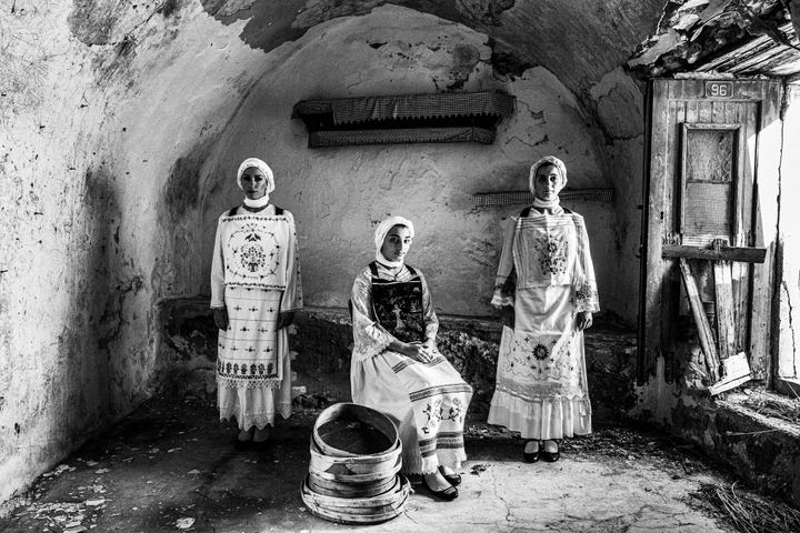 Three women wearing the local costumes of Lithi on the island of Chios, standing inside an old local house.