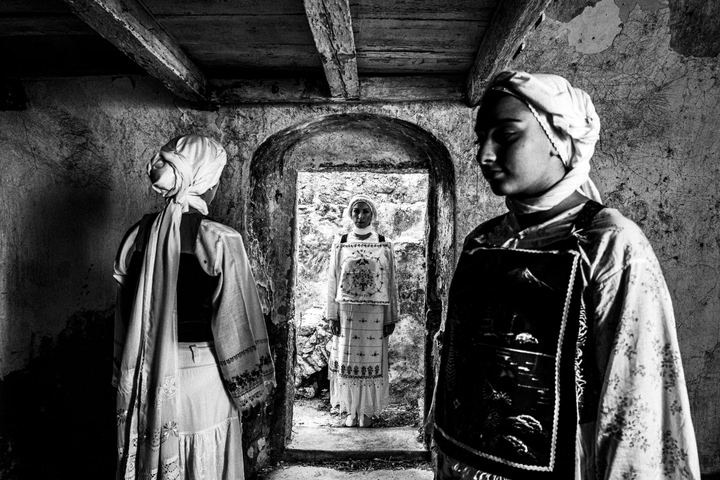 Three women wearing the local costumes of Lithi on the island of Chios, standing inside an old local house.