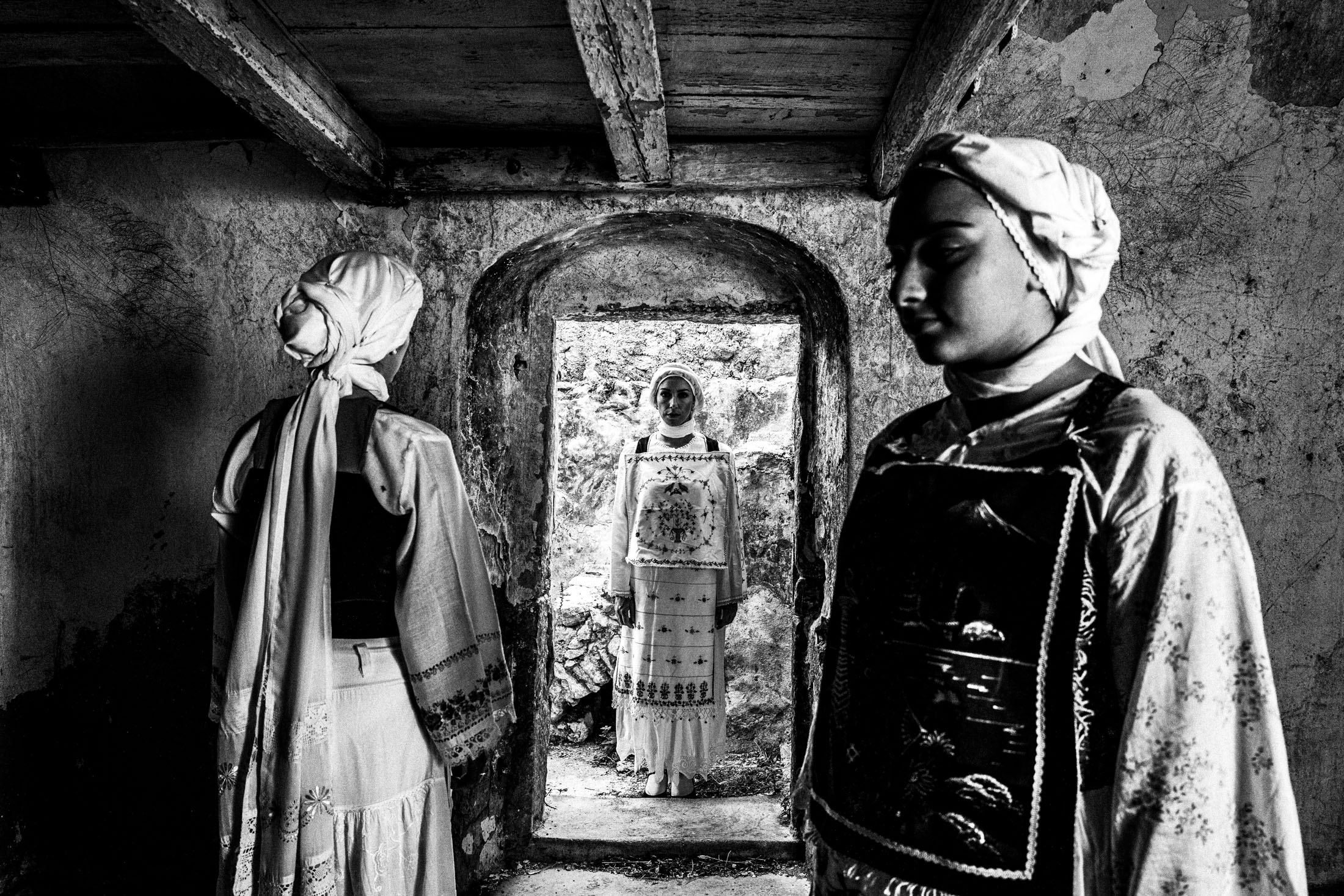Three women wearing the local costumes of Lithi on the island of Chios, standing inside an old local house.