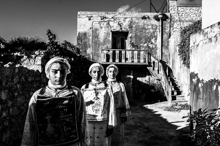 Three women wearing the local costumes of Lithi, standing in the sun outside a local house