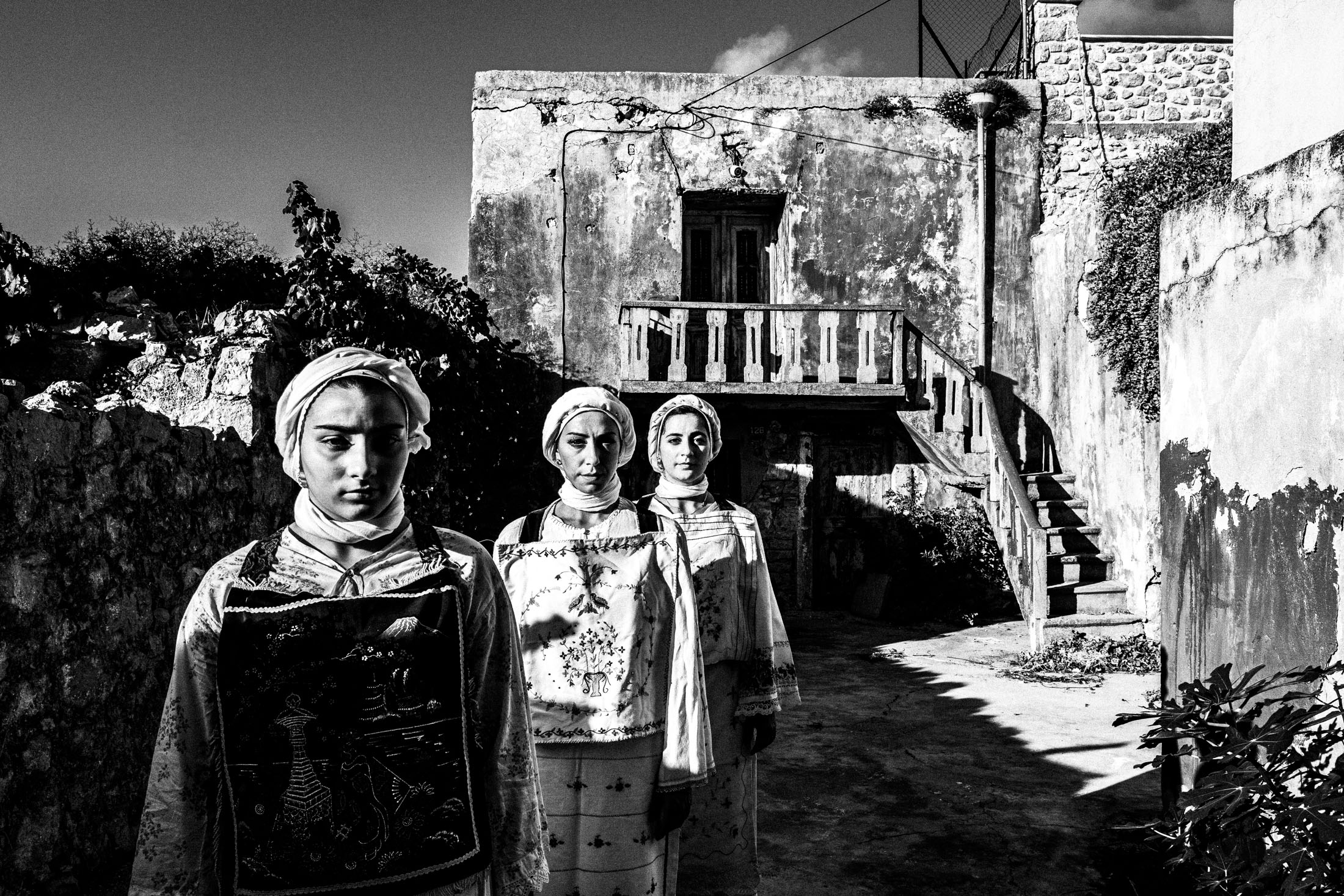 Three women wearing the local costumes of Lithi, standing in the sun outside a local house