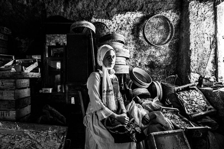 A woman wearing the local dress of Nenita, Chios, sitting inside a warehouse that stores mastic and related tools.