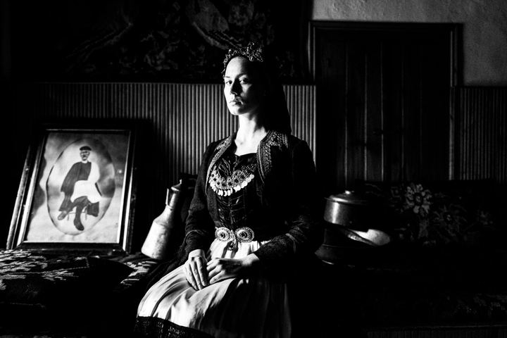 A woman wearing the local costume of Vovoussa, sitting inside a local house by the window