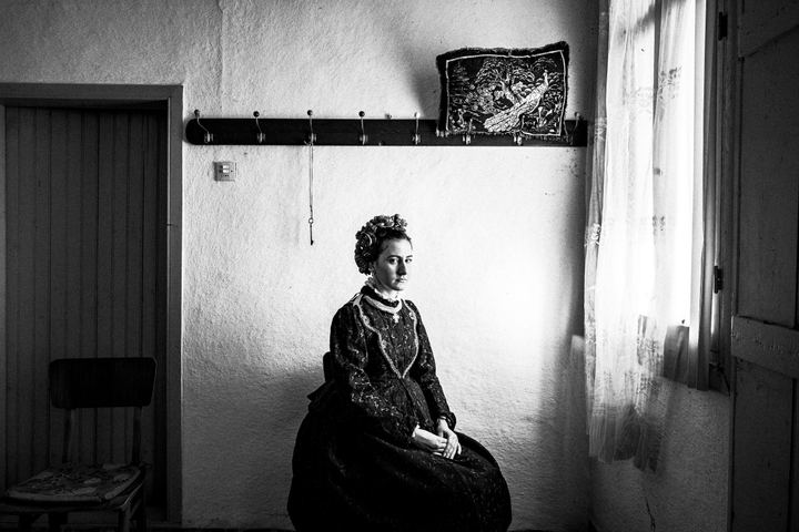 Woman wearing the local costume of Nea Vyssa in Evros, sitting by the window inside a local home