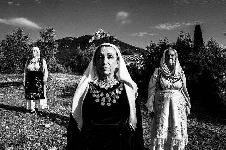 Three women wearing the local costumes of Perachora, Corinth, at a local hill with a mountain top behind them