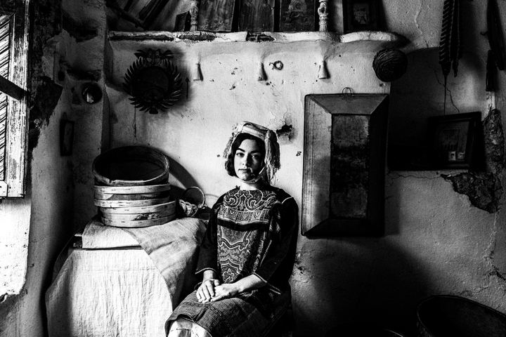 A woman wearing the local costume of Lithi, seated inside a local house by a window