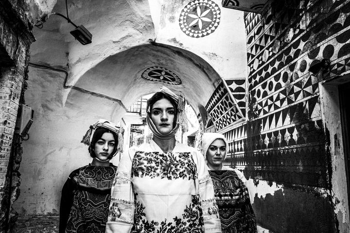 Three women in an alley at Pyrgi wearing the local traditional costumes before the famous Xisto geometrical shapes