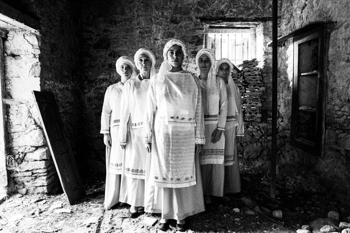 Five women wearing the local costumes of Ververato, standing in formation inside a local house