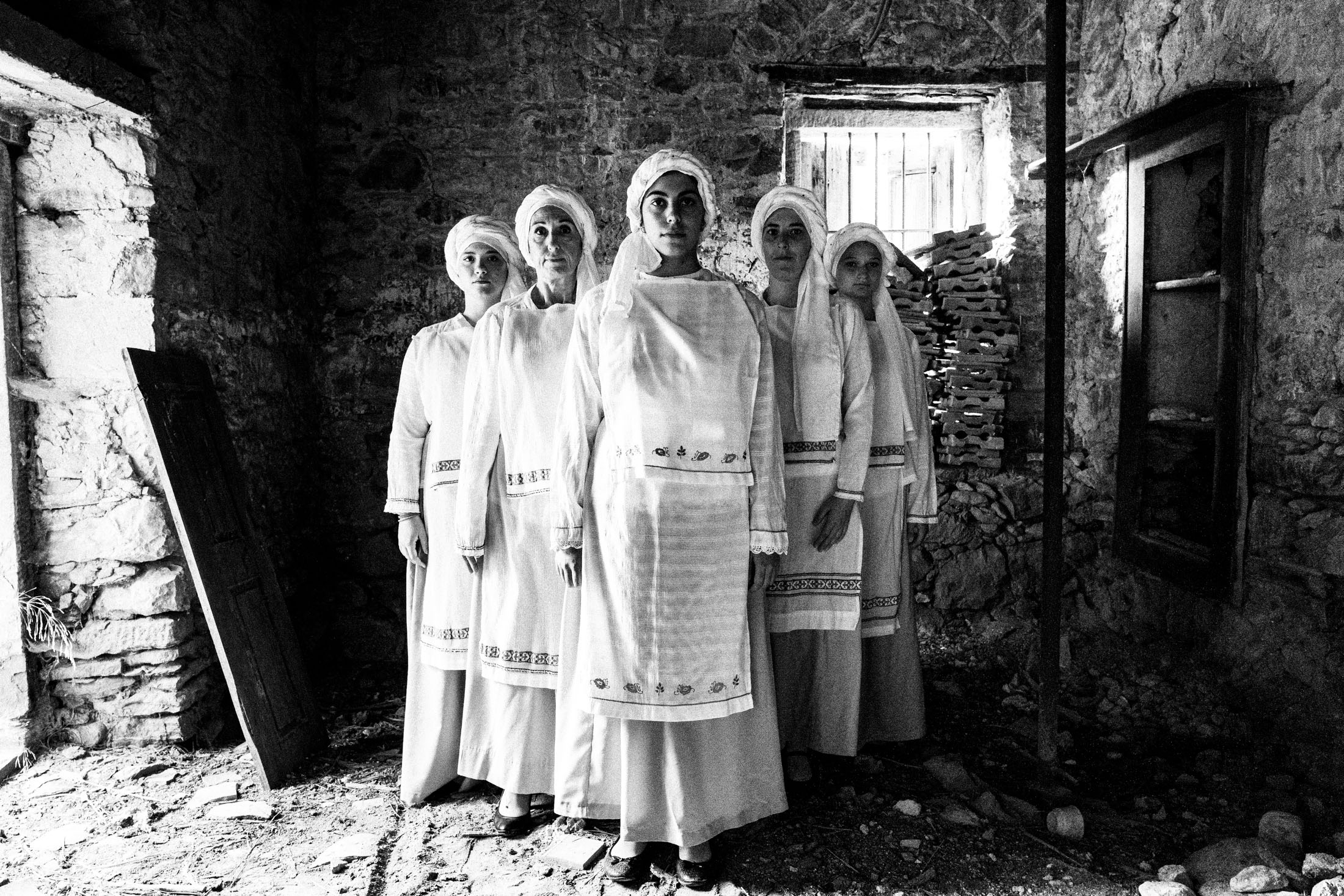 Five women wearing the local costumes of Ververato, standing in formation inside a local house