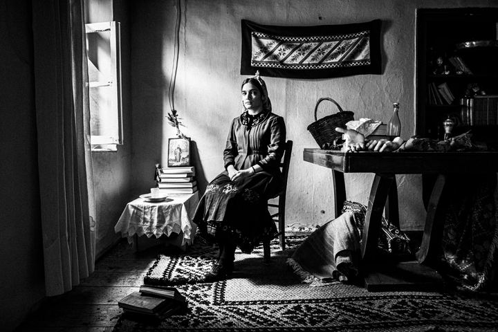 A women wearing the costume of Divri, Lamia, sitting inside a local house by the window