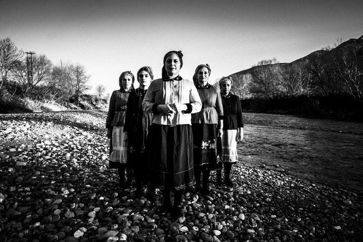 Women wearing the local costumes of Divri, standing in an arrow formation at a local river bank