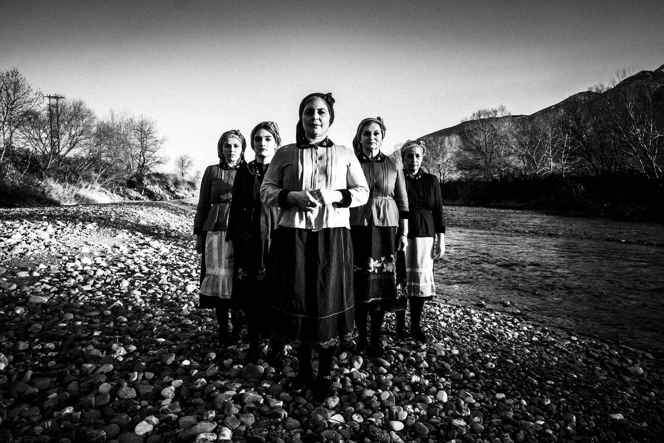 Women wearing the local costumes of Divri, standing in an arrow formation at a local river bank
