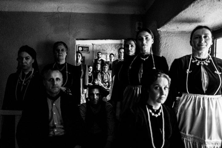 A group of people across generations, wearing the costumes of Polypotamos, Florina, inside a local house