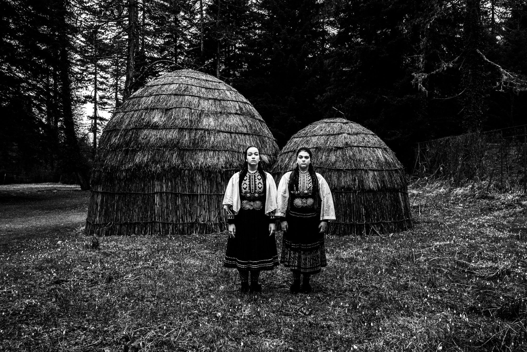 Two young women wearing the Sarakatsani nomadic group costumes, posing at Gyftokampos, Epiurs, by Sarakatsani traditional straw huts