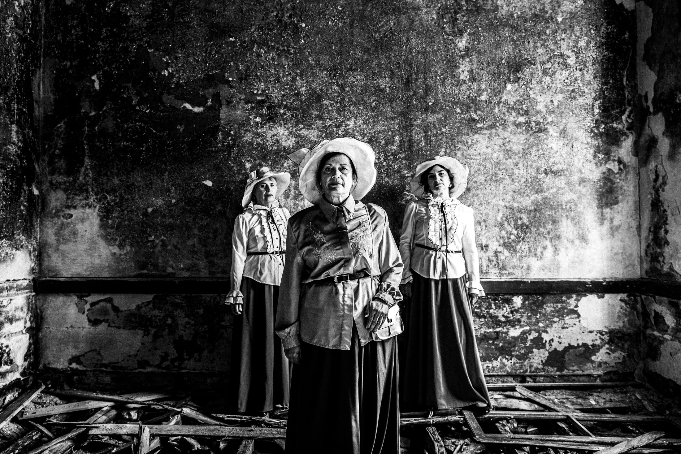 Three women in the local urban dresses of Kofinas in Chios, standing inside the local abandoned leprosarium