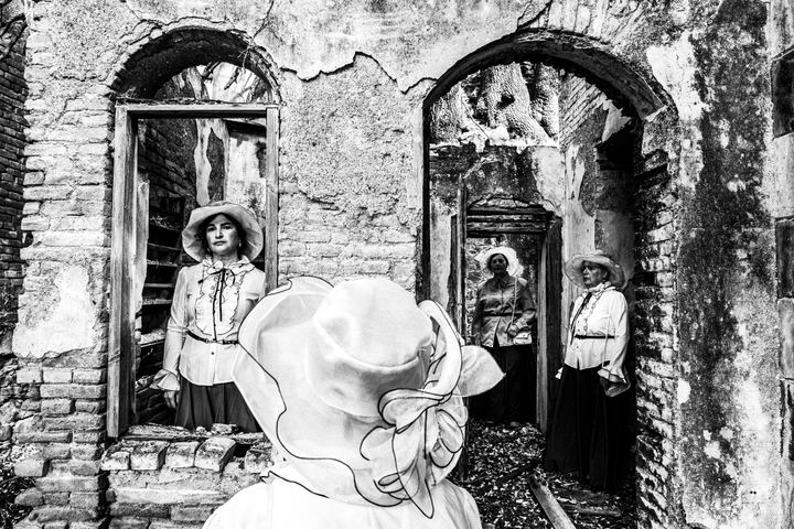 Four women standing amongst the ruins of a local leprosarium, wearing the urban dresses of Kofinas, Chios.