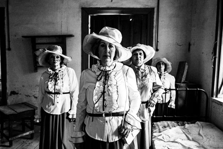 Four women standing amongst the ruins of a local leprosarium, wearing the urban dresses of Kofinas, Chios.