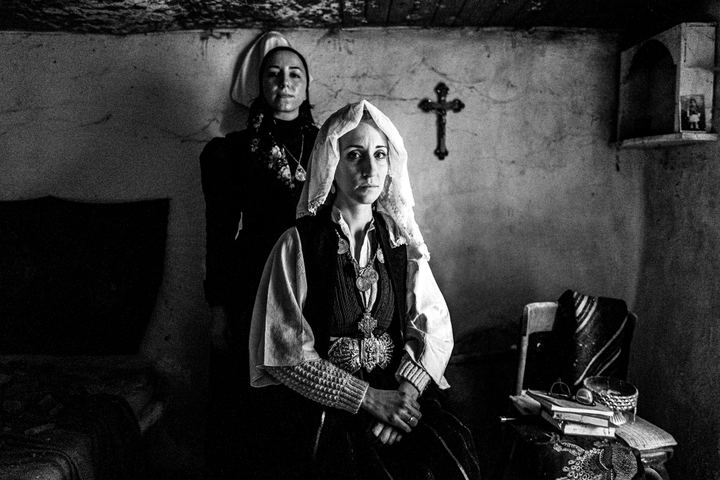 A bride and another woman, wearing the local costumes of Ermakia, posing by a crucifix, inside a local abandoned house, Ptolemaida, Macedonia