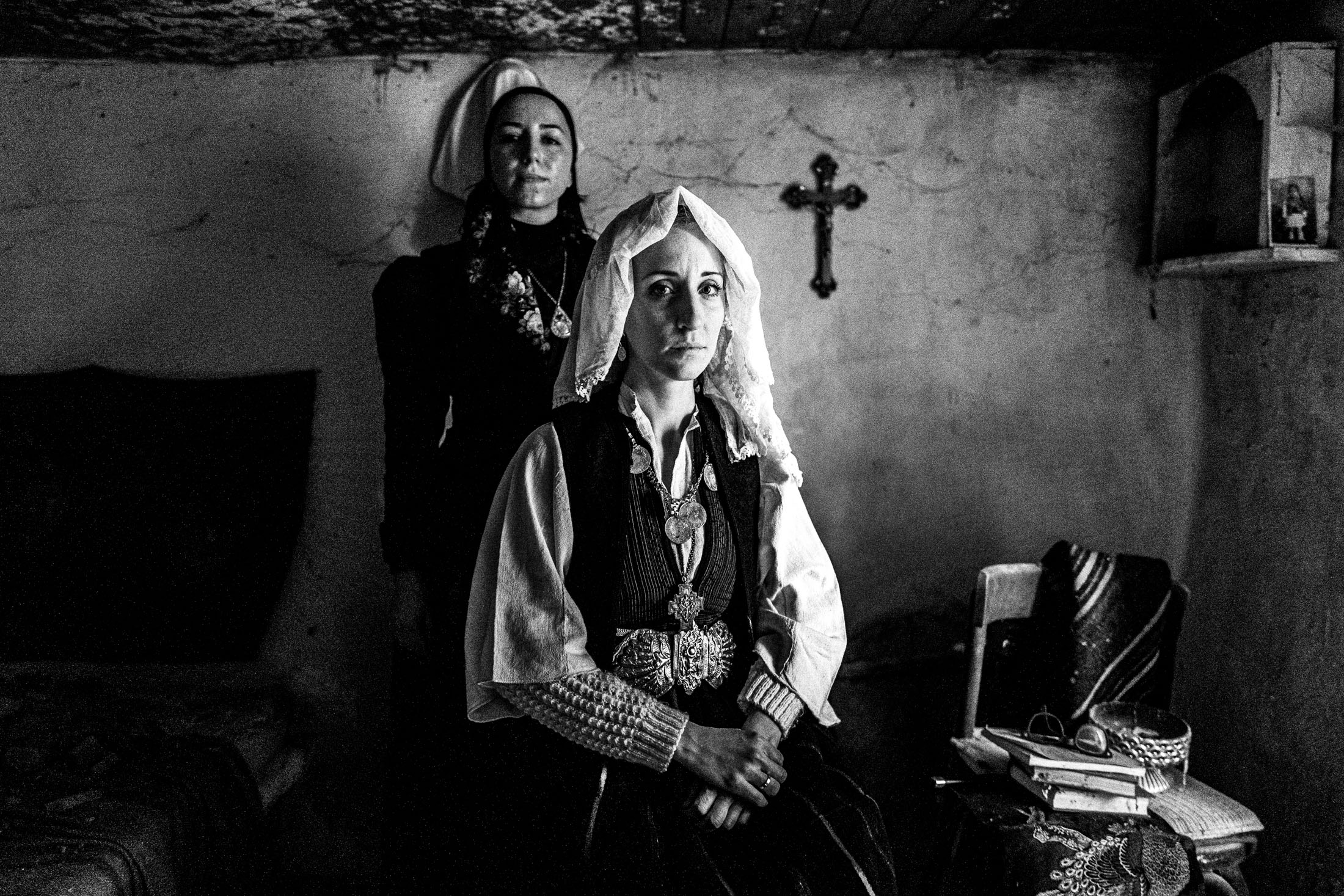 A bride and another woman, wearing the local costumes of Ermakia, posing by a crucifix, inside a local abandoned house, Ptolemaida, Macedonia