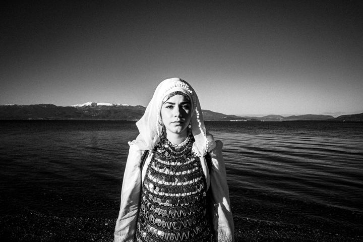 A young woman againsta the sun wearing the costume of Atalanti standing by the sea of Kammena Vourla