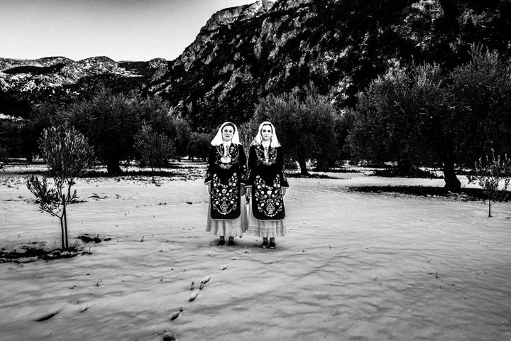 Two women wearing the costumes of Martino, standing on the snow one next to each other at an olive grove