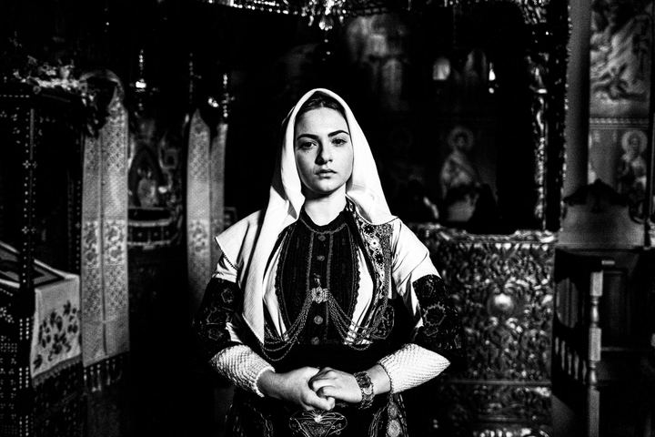 A woman wearing the local costume of Kladorachi in Florina, posing for a close-up portrait inside a local orthodox church