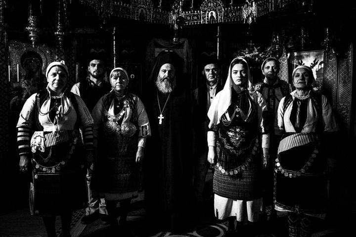 People wearing the local costumes of Klardorrachi, Florina, standing around a priest inside a local church
